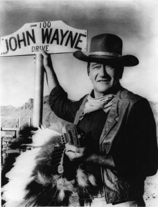 Fox Photos/Getty Images American actor John Wayne stands by the street sign honoring his name in Prescott, Ariz. The film star "was one of the defining Americans of the 20th century," says critic John Powers.
